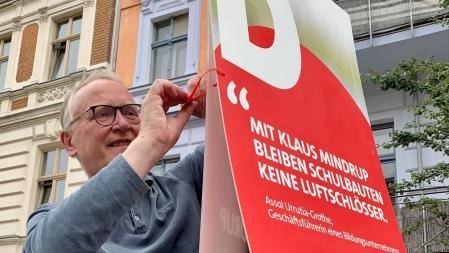 Klaus hängt eines seiner Plakate an eine Laterne auf.