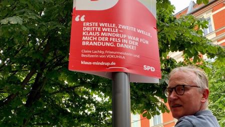 Klaus hängt das Plakat mit dem Zitat von Claire Lachky auf, Friseurmeisterin und Besitzerin von Vokuhila