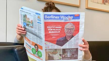 Junge Frau liest die Berliner Woche mit der Anzeige von Klaus Mindrup